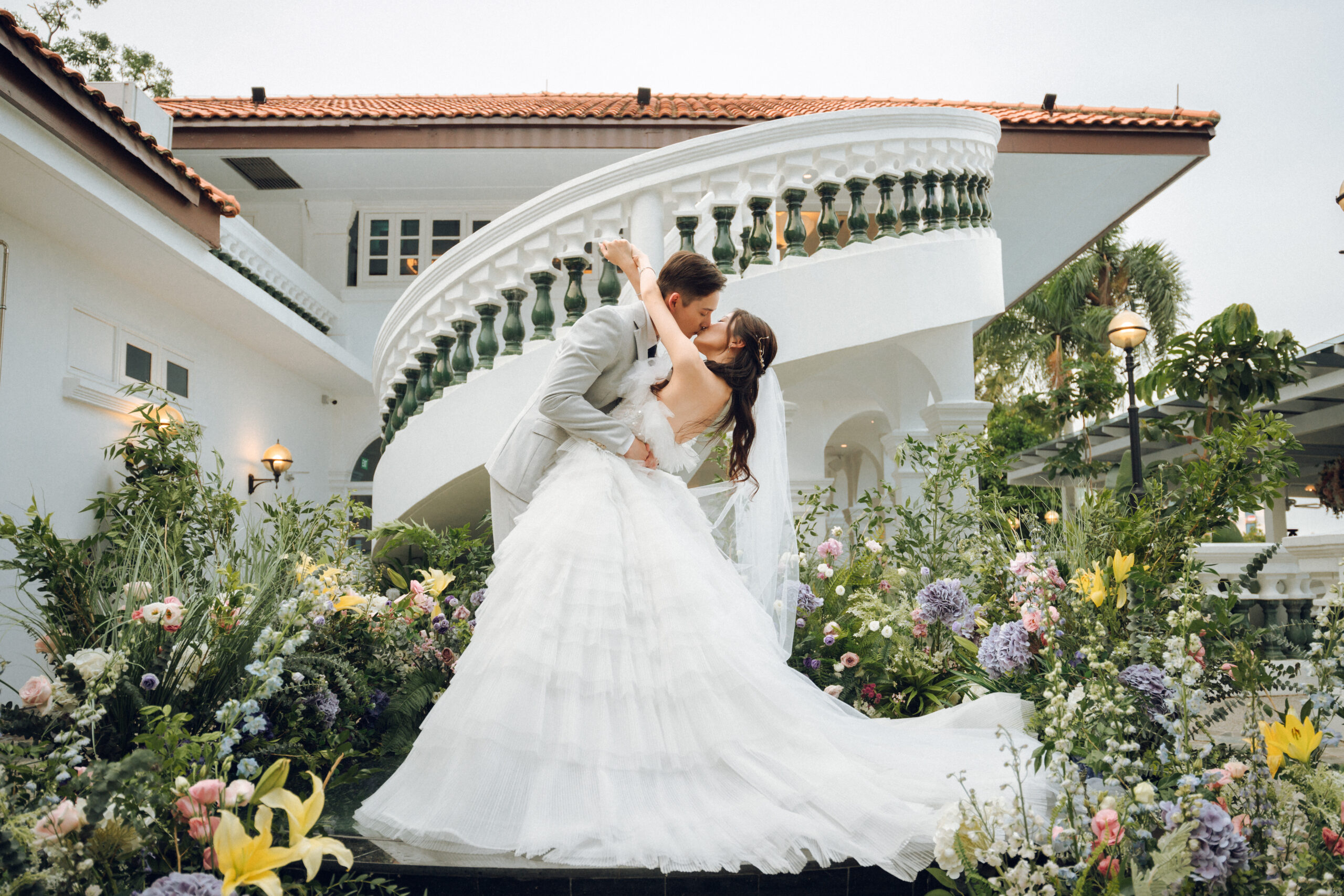 Couple kissing on the colonial mansion staircase at 1-Flowerhill, framed by garden florals