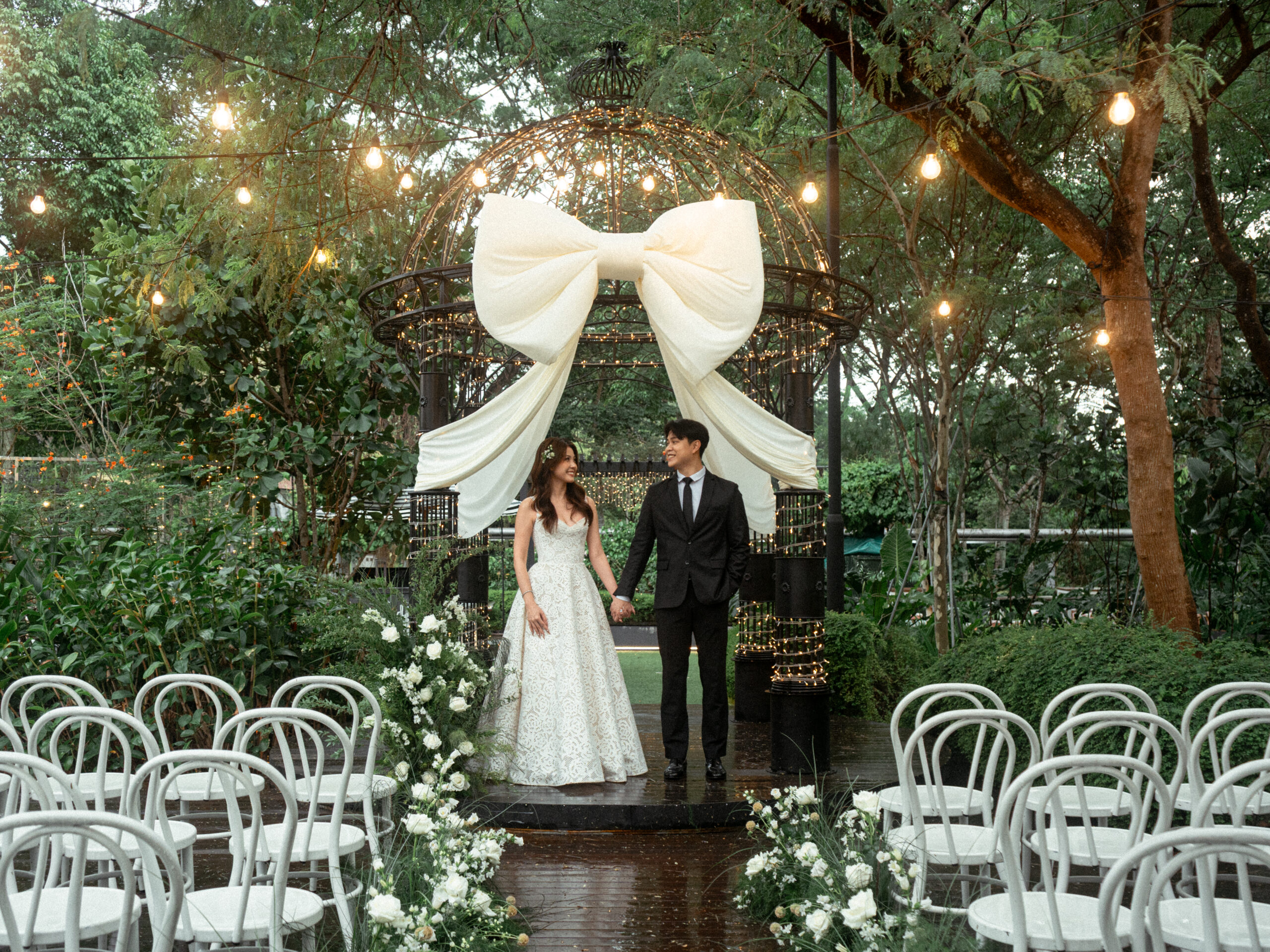 Bride and groom at a garden gazebo ceremony aisle dressed with a large ivory bow